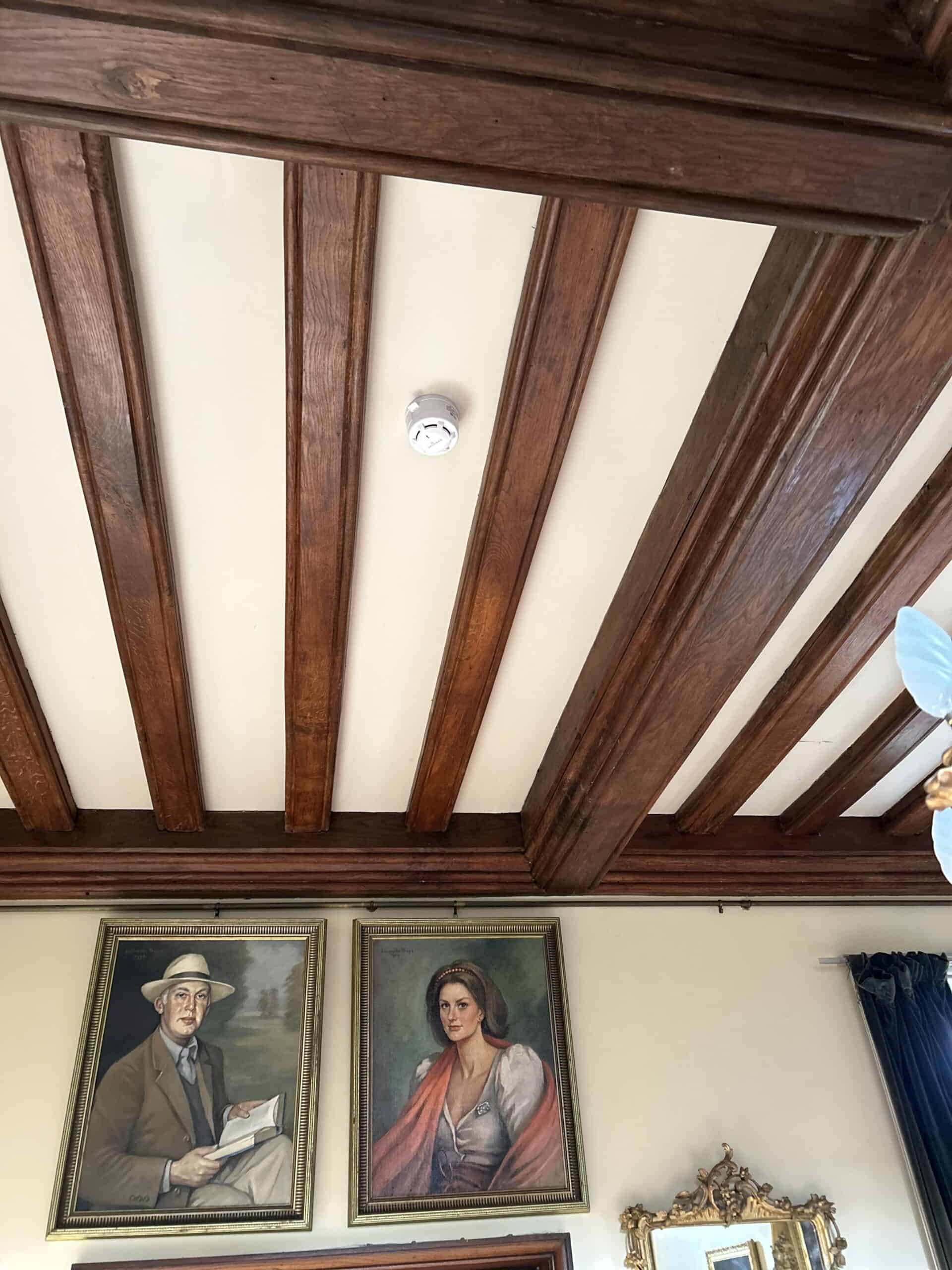 Ceiling beams with two portraits in room.