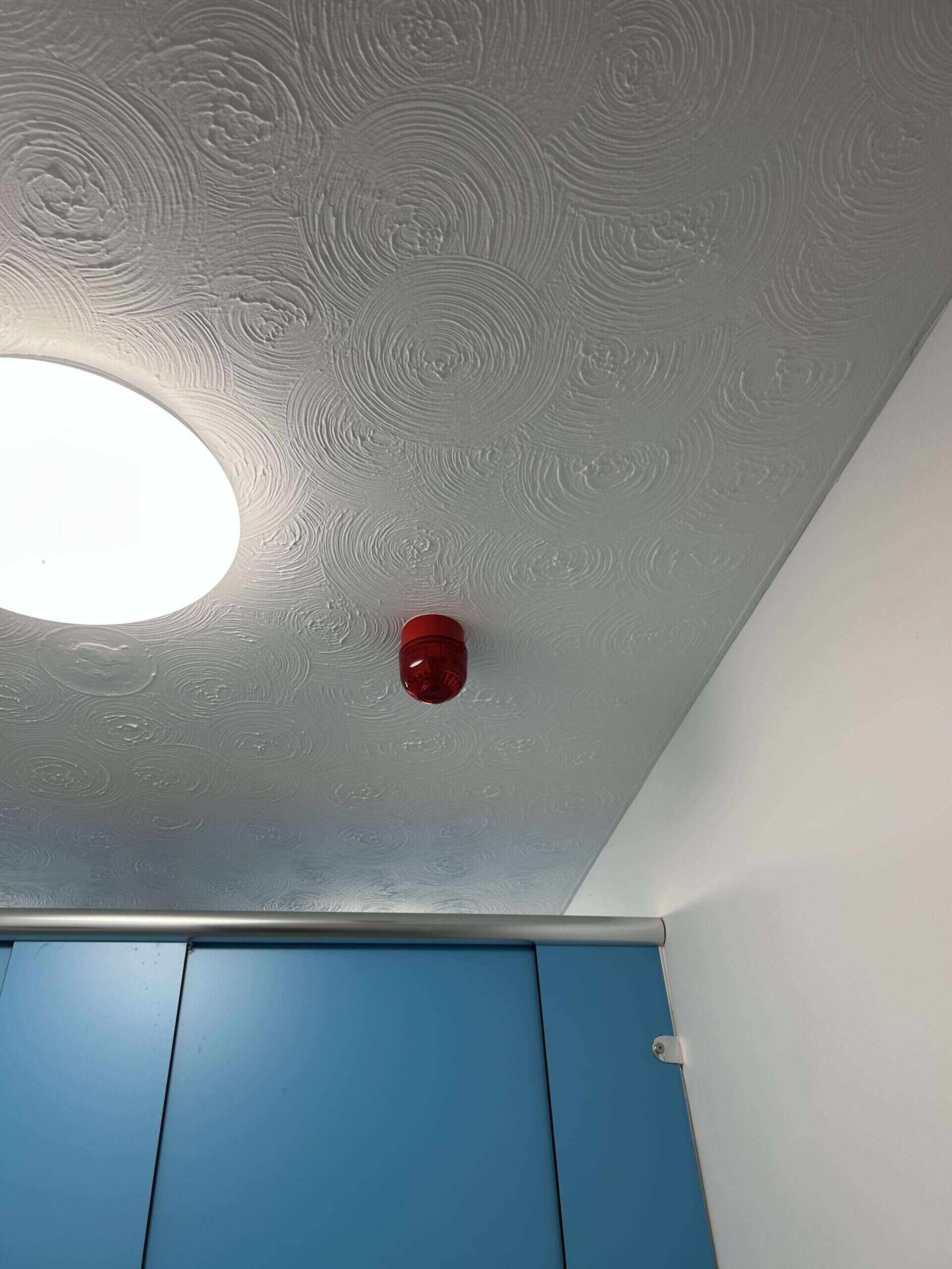Red fire alarm on textured ceiling with light.